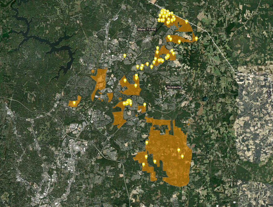 A satellite map of the region between Wake Forest and Rolesville, North Carolina, illustrating the boundaries of the "Neuse North Area Plan." Large, irregular sections of land are highlighted in translucent orange, representing the controversial "Orange Zone" proposed for development. These orange areas surround and encroach upon residential pockets, including Chesterfield Village. Numerous yellow pins mark specific properties or locations of interest within these zones, likely representing affected homes or areas currently being studied. The map highlights the proximity of these zones to the dense greenery of the Neuse River tributary system.