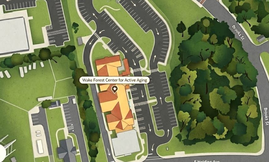 The image shows the main center building with an orange roof highlighted by a label and star icon, surrounded by extensive parking lots with directional arrows, green spaces, and a dense wooded area to the east. Streets named E Holding Ave and Brooks St border the site. The image shows the main center building with an orange roof highlighted by a label and star icon, surrounded by extensive parking lots with directional arrows, green spaces, and a dense wooded area to the east. Streets named E Holding Ave and Brooks St border the site.
