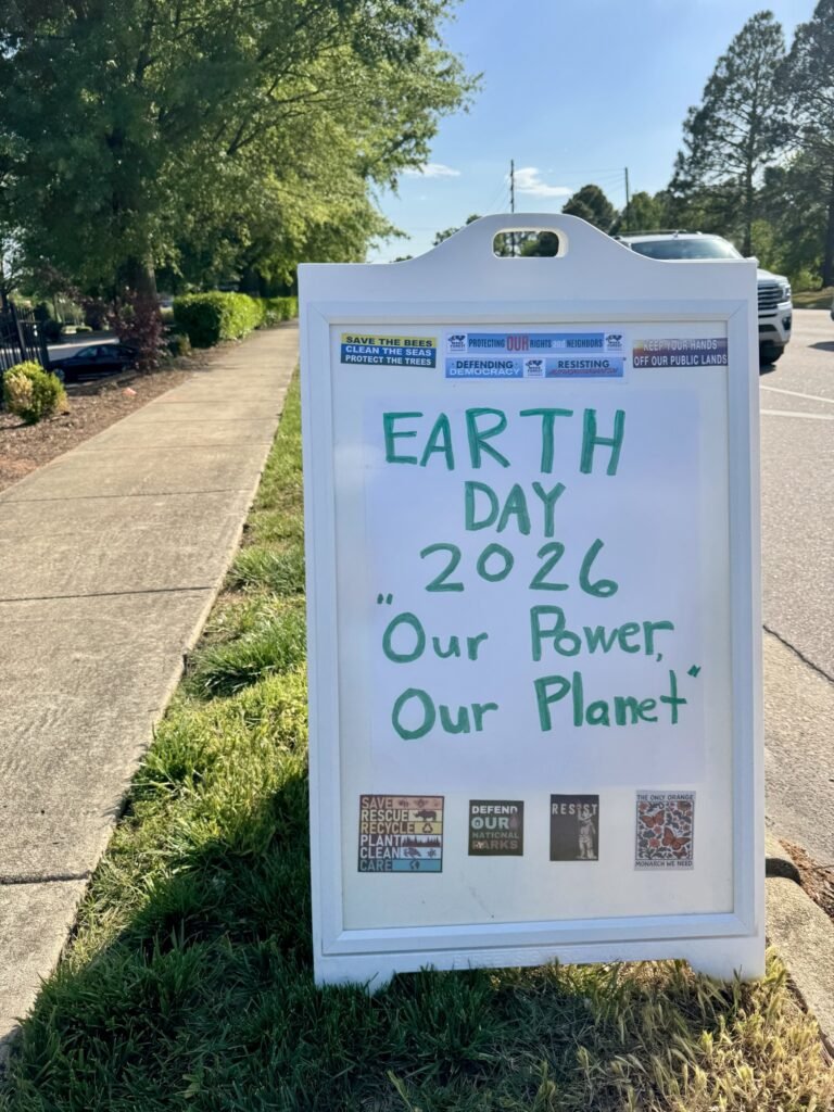 Earth Day 2026 protest sign reading Our Power Our Planet at Rogers Rd intersection