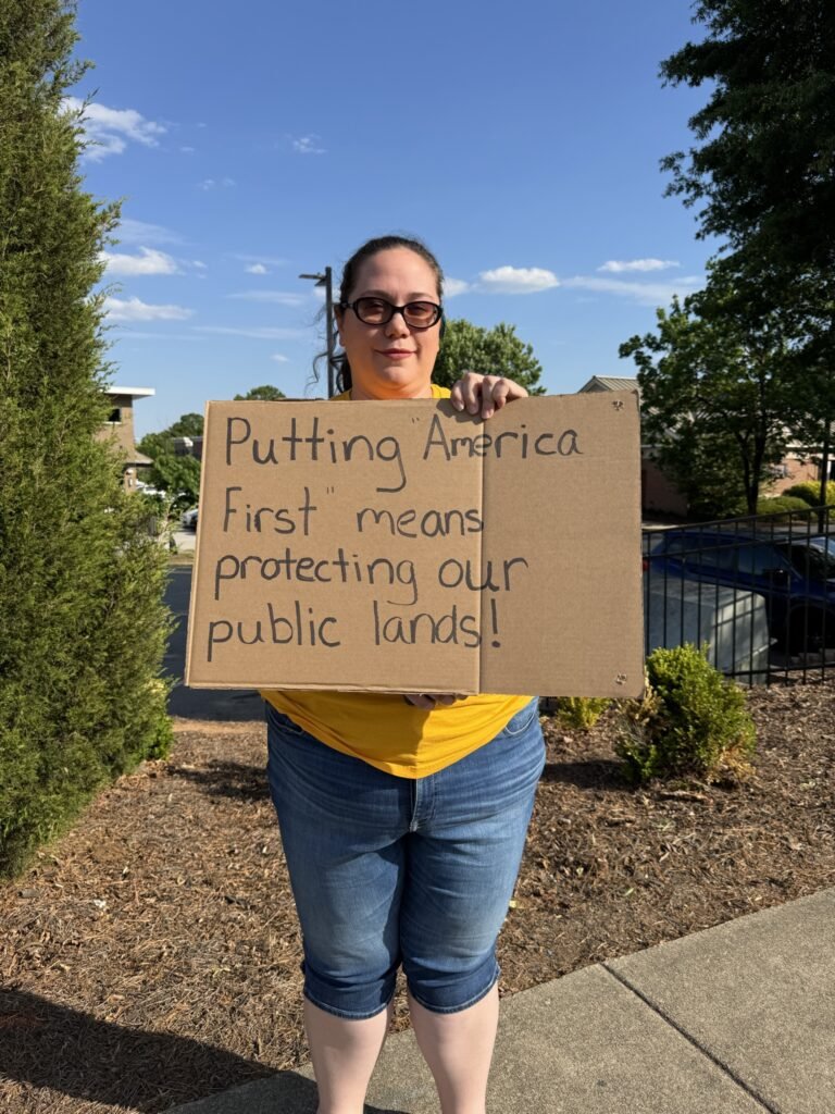 Wake Forest Earth Day protest - activist holding sign reading Putting America First means protecting our public lands
