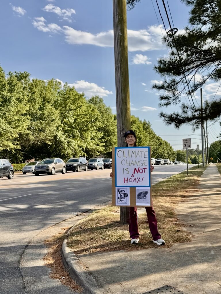 Activist holding Climate Change is Not a Hoax sign at Rogers Rd Earth Day protest