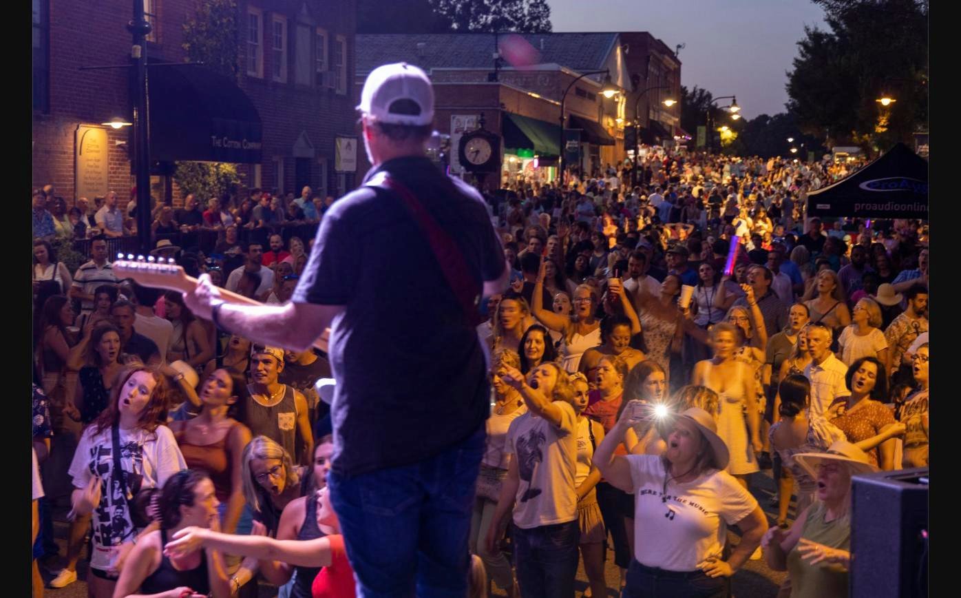 Guitarist performs on stage during Friday Night on White, facing a packed crowd on South White Street in downtown Wake Forest